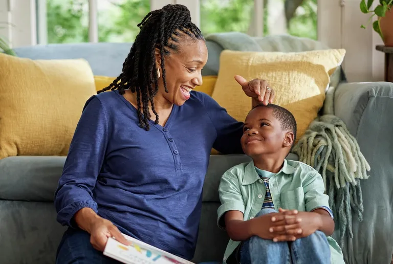 An adult and a child sitting together on a living room floor looking at a book.