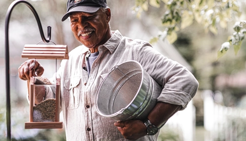 Senior man refilling bird feeder in garden