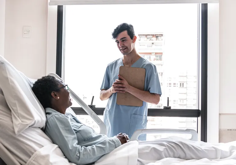 Male Medical Provider Speaks To Patient While Holding Clipboard