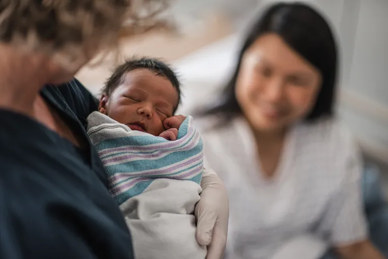 Newborn Baby Being Held While Mother Looks On