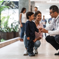 Doctor checking the pulse of a young boy standing with his mother.