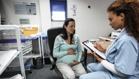 Doctor giving prescription to pregnant woman at desk