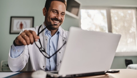 Happy male doctor surfing the Internet on a computer in the office at hospital