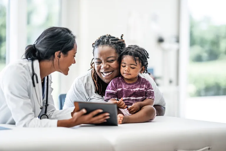 Pediatrician shows digital tablet to mother of toddler