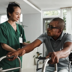 A home health provider assists a member transitioning from his wheel chair to using a walker.