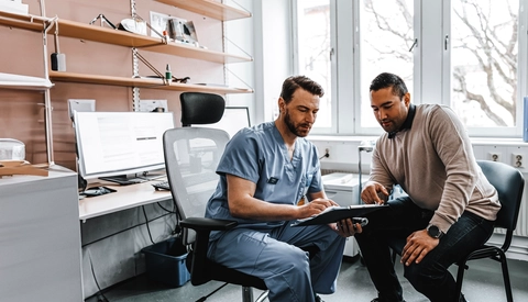 Male medical expert discussing reports with male patient during visit at hospital