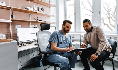 Male medical expert discussing reports with male patient during visit at hospital 