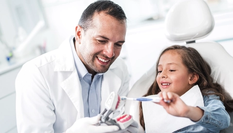 Male Dentist Showing Young Girl How To Brush Her Teeth