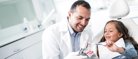 Male Dentist Showing Young Girl How To Brush Her Teeth