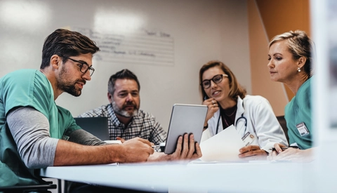 A group of hospital staff sitting around a meeting table reviewing information on a tablet.