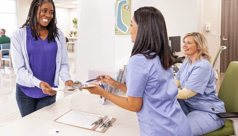 Female receptionist gives clipboard to patient in medical lobby